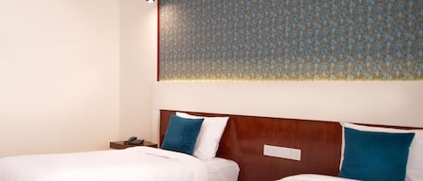 Een hotelkamer met twee enkele bedden, een houten hoofdbord, een nachtkastje en een behang met een patroon.