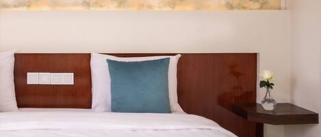A neatly made bed with white and blue bedding, a wooden headboard, and a small bedside table with a vase of flowers.