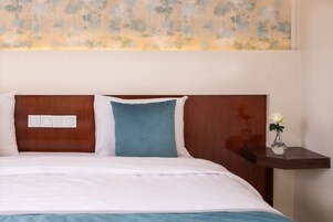 Una cama bien hecha con ropa de cama blanca y azul, un cabecero de madera y una mesita de noche con un florero.