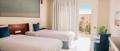 Habitación de hotel con dos camas, un ventanal con cortinas, vistas al exterior y una zona de estar con una silla y una planta.