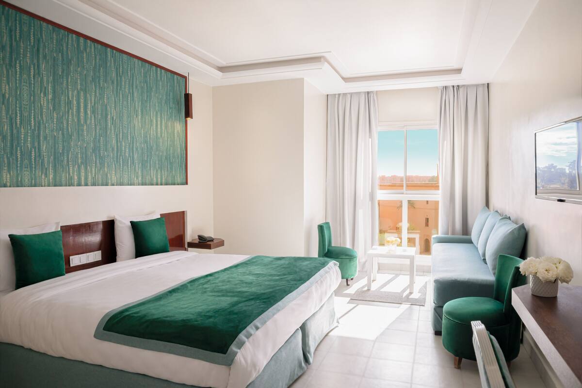 A hotel room with a large bed, a sofa, a chair, and a view of the city.