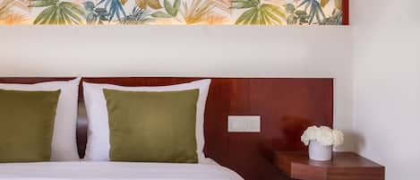 A hotel room with a bed, two pillows, a nightstand, and a wall with a tropical leaf pattern.
