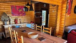 Interior de una cabaña de madera con una mesa de comedor, sillas, una zona de cocina y una acogedora sala de estar.
