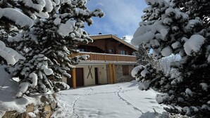 Una cabaña de madera con fachada de piedra y un balcón de madera, sobre un paisaje cubierto de nieve.