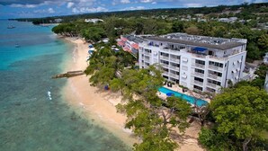 An aerial view of a beachfront hotel with a pool, beach, and clear turquoise waters. - Beachfront luxury modern 2-bed apt with pool by BSL Rentals (Paynes Bay)