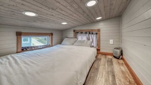 Un dormitorio con cama, techo de madera y ventana con cortinas.