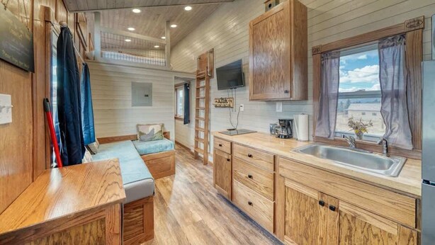 Cocina compacta para autocaravana con armarios de madera, un lavabo y una ventana con cortinas.