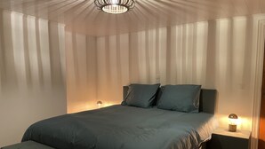 A bedroom with a bed, two bedside tables, a bench, and a ceiling light fixture.