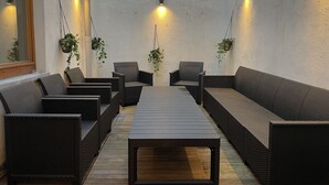 A modern outdoor seating area with wicker furniture and hanging plants, featuring a wooden table and wall-mounted lighting.