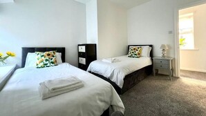 A hotel room with two beds, a small bedside table with a lamp, and a door leading to a bathroom. - Angel Lane Apartment. Alnwick Town Centre (Alnwick)