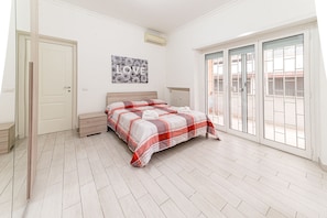 A bedroom with a bed, a bench, a radiator, and a sliding glass door to a balcony.