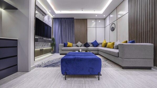 A modern living room with a grey sofa, blue and yellow cushions, a blue ottoman, and a marble wall.