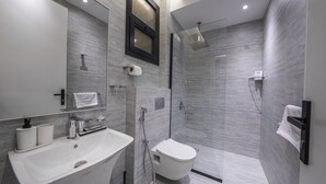 A modern bathroom with a white sink, mirror, and toilet. It features a glass-enclosed shower area with a handheld showerhead. - Mabaat - Al Aqiq - 504 (Riyadh)