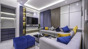 A modern living room with a grey sofa, blue and yellow cushions, a flat-screen TV, and a built-in air conditioning unit.