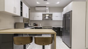A modern kitchen with a wooden table and two chairs, stainless steel appliances, and white cabinetry. - Mabaat - Al Aqiq - 504 (Riyadh)
