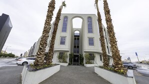 A building with a central arched entrance, flanked by tall palm trees, and a paved walkway leading to the entrance. - Mabaat - Al Aqiq - 504 (Riyadh)
