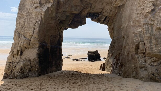 Une formation rocheuse naturelle présentant une ouverture en forme de grotte sur une plage de sable.