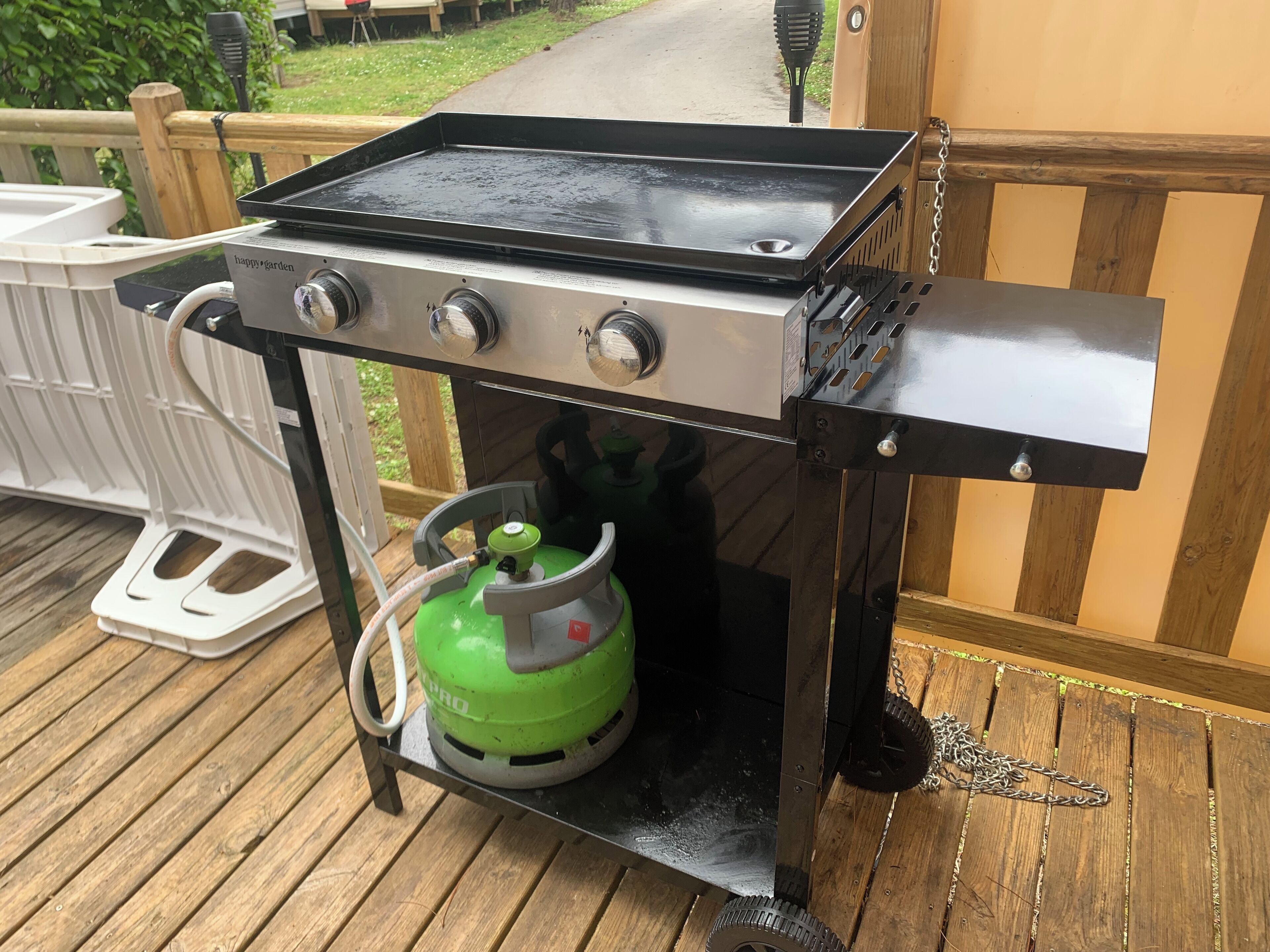 Un barbecue au gaz portable doté d’une surface de cuisson noire, de trois boutons et d’une bouteille de propane verte.