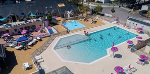 Ein Schwimmbecken mit Liegestühlen und Sonnenschirmen, umgeben von einem eingezäunten Bereich mit Lounge-Möbeln und einem Gebäude im Hintergrund.