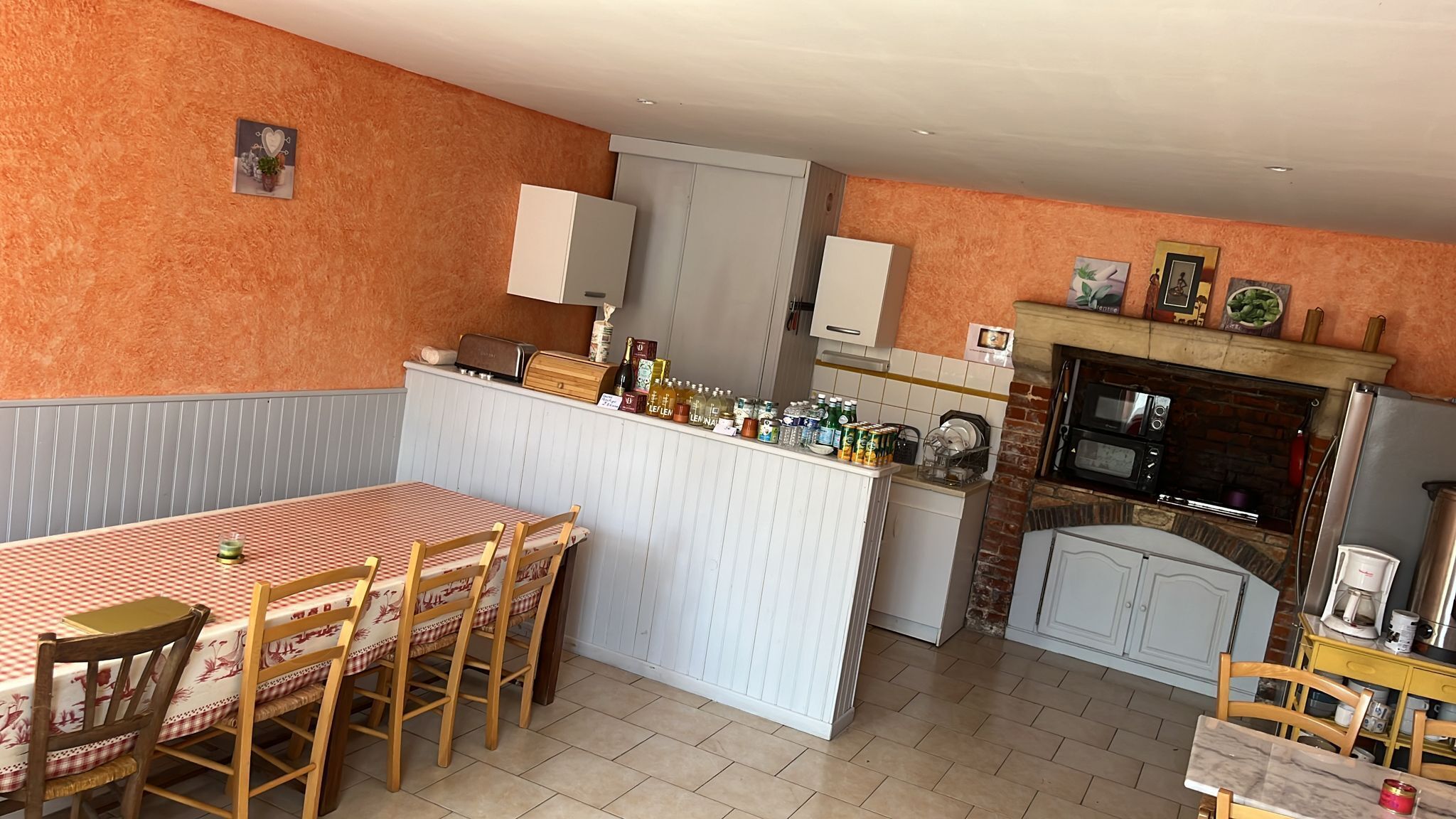 Een compacte keuken met een eethoek, met een geruit tafelkleed, houten stoelen, een inbouwoven en een koelkast.