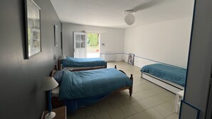 Une chambre avec deux lits, un bureau, une chaise, une lampe et une porte donnant sur un balcon.