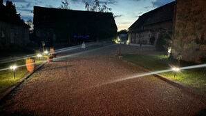 Un chemin pavé, bordé de chaque côté de plantes en pot, mène à un bâtiment dont le toit est recouvert de chaume.