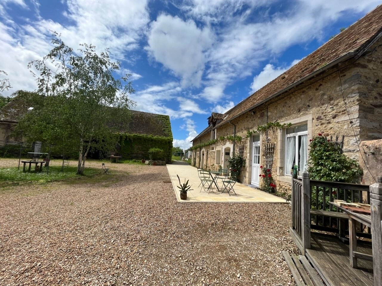 Un bâtiment en pierre avec une allée en gravier, des sièges à l’extérieur et une terrasse en bois.