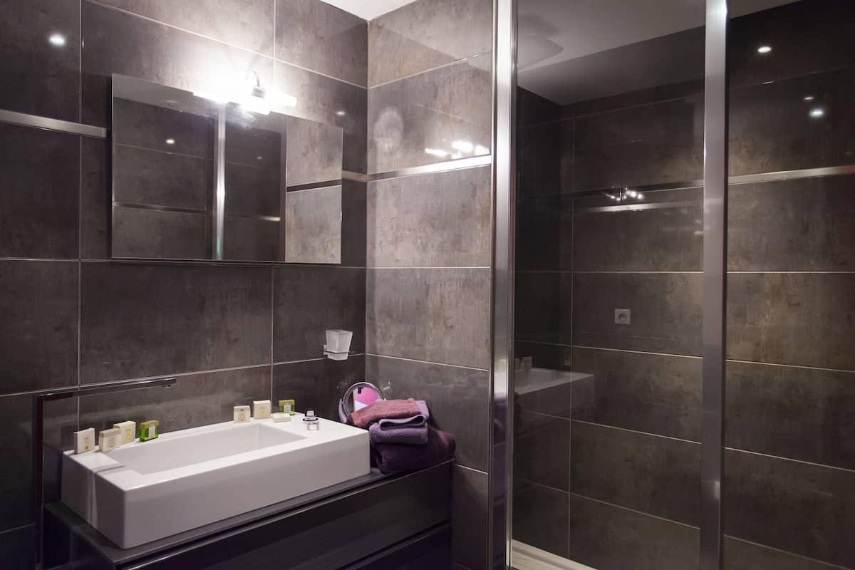 A modern bathroom with a large mirror, a white sink, and a glass shower enclosure.