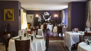 A dining area with round tables, chairs, and white tablecloths. There are wall-mounted light fixtures and a decorative mirror. - Hôtel la Source Bleue (Gudmont)