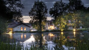 A lakeside hotel with multiple buildings, a reflective pond, and surrounding trees. - Hôtel la Source Bleue (Gudmont)