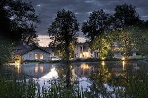 Hotel junto al lago con varias construcciones, un estanque que refleja el paisaje y árboles circundantes.