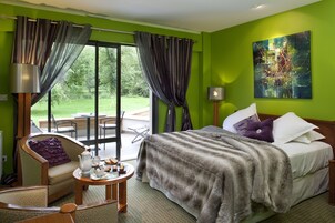 Habitación de hotel con cama, una silla, una mesa con juego de té y vistas al exterior.