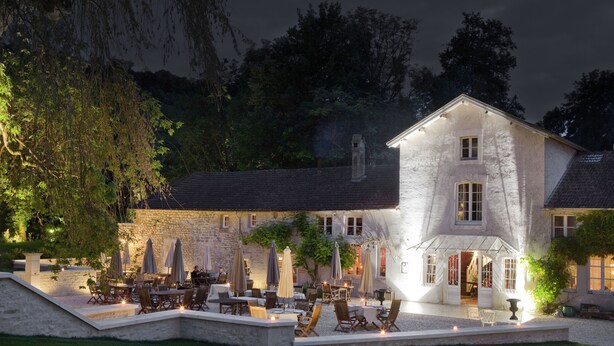 A stone building with a patio area featuring outdoor seating and umbrellas. - Hôtel la Source Bleue (Gudmont)