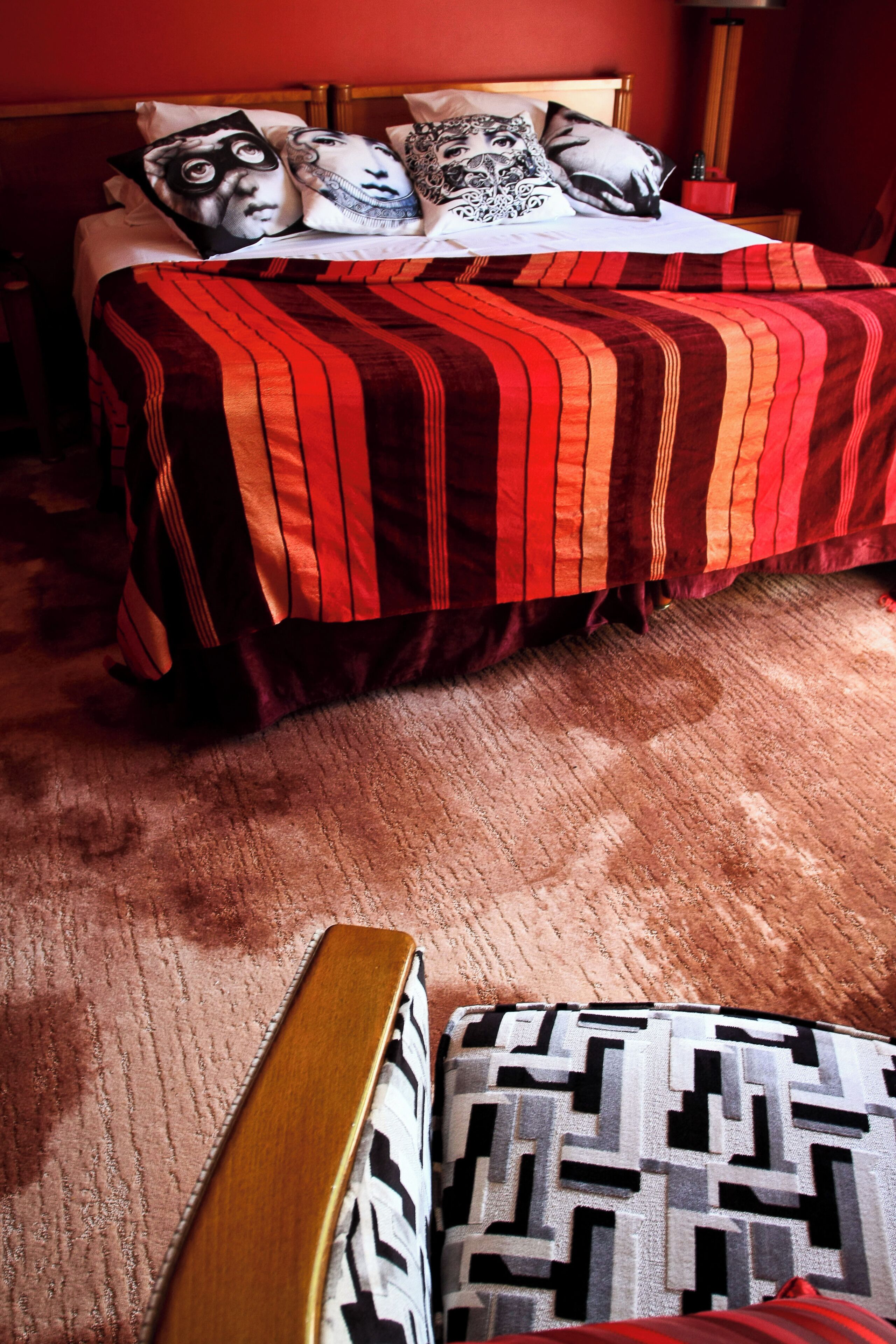 A bed with a red and black striped bedspread, multiple pillows with various patterns, and a wooden headboard.