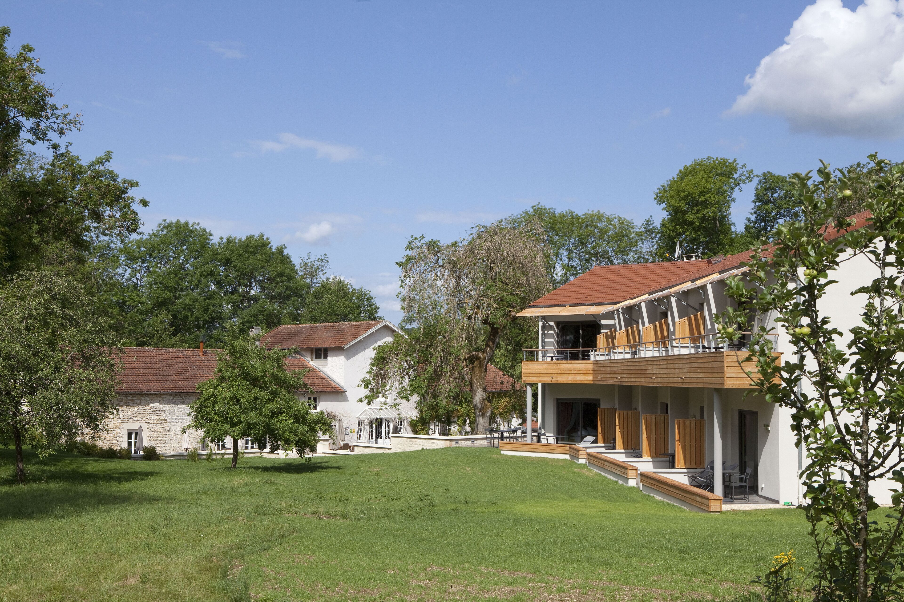 A modern building with a wooden balcony, surrounded by a well-maintained lawn and trees.