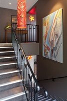 Una escalera con barandilla de metal, una lámpara decorativa roja y un cuadro abstracto de gran tamaño en la pared.