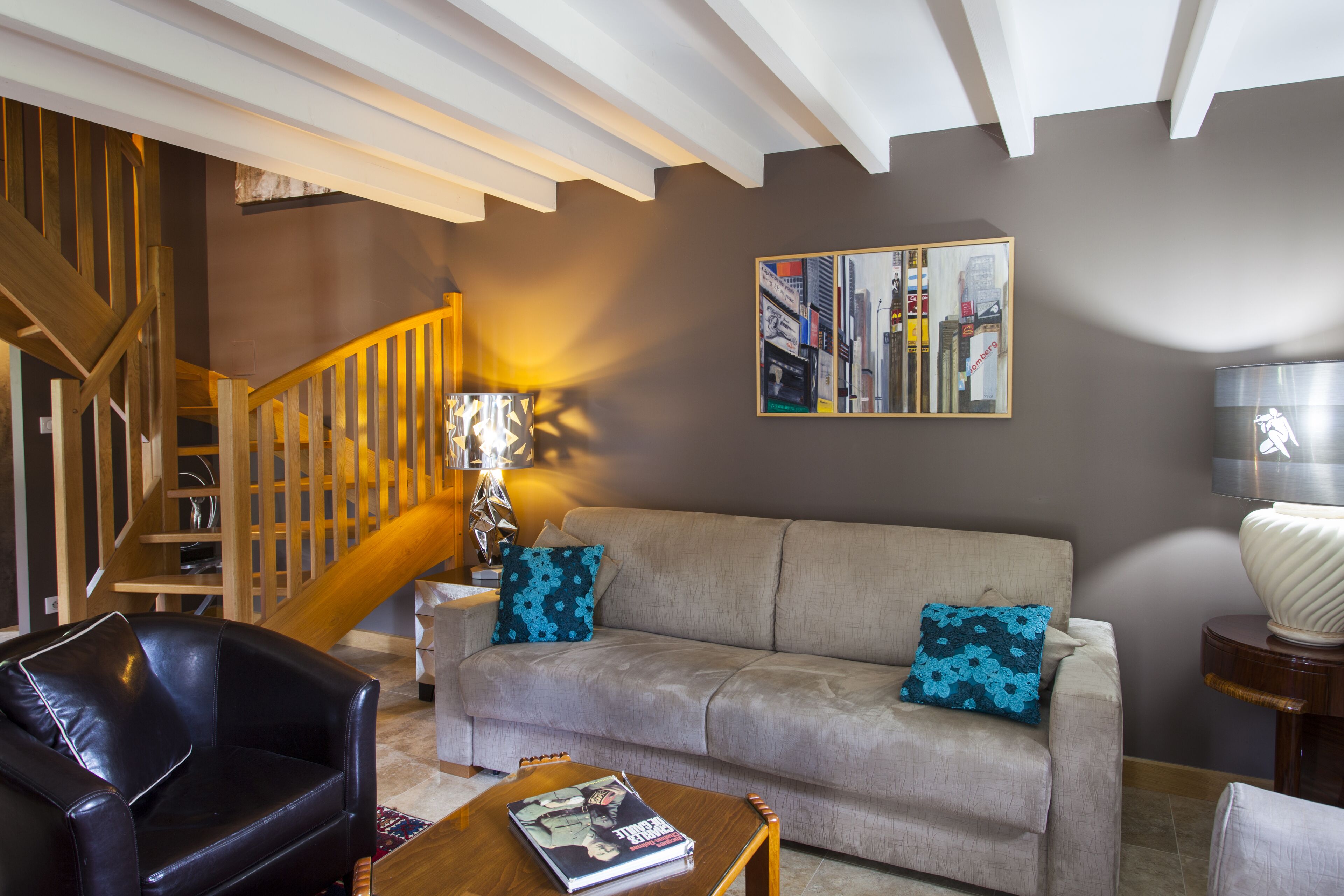 A living room with a sofa, a black leather chair, a wooden coffee table, and a staircase.
