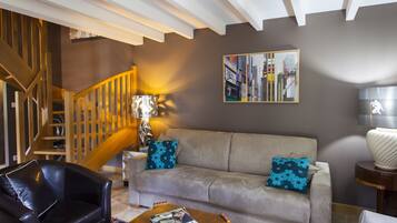 A living room with a sofa, a black leather chair, a wooden coffee table, and a staircase.