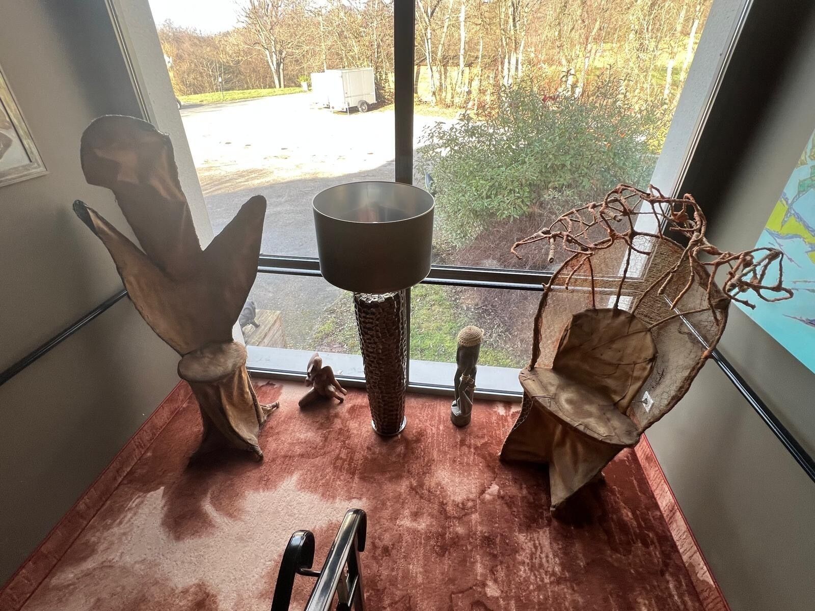 A room with a large window, a metal sculpture, and a rustic wooden chair.