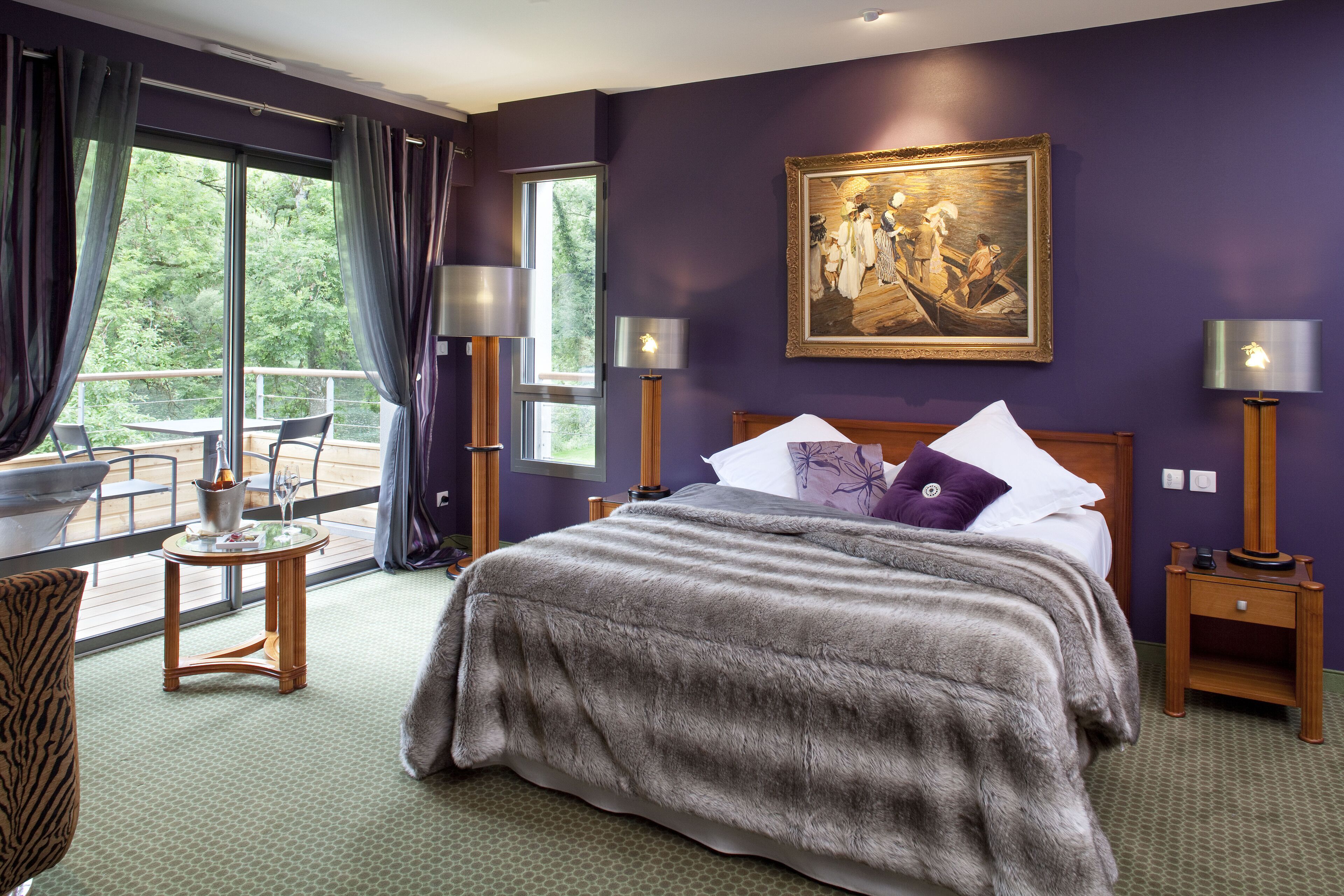 A room with a large bed, a painting on the wall, and a balcony with a table and chairs.