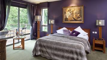 A room with a large bed, a painting on the wall, and a balcony with a table and chairs.