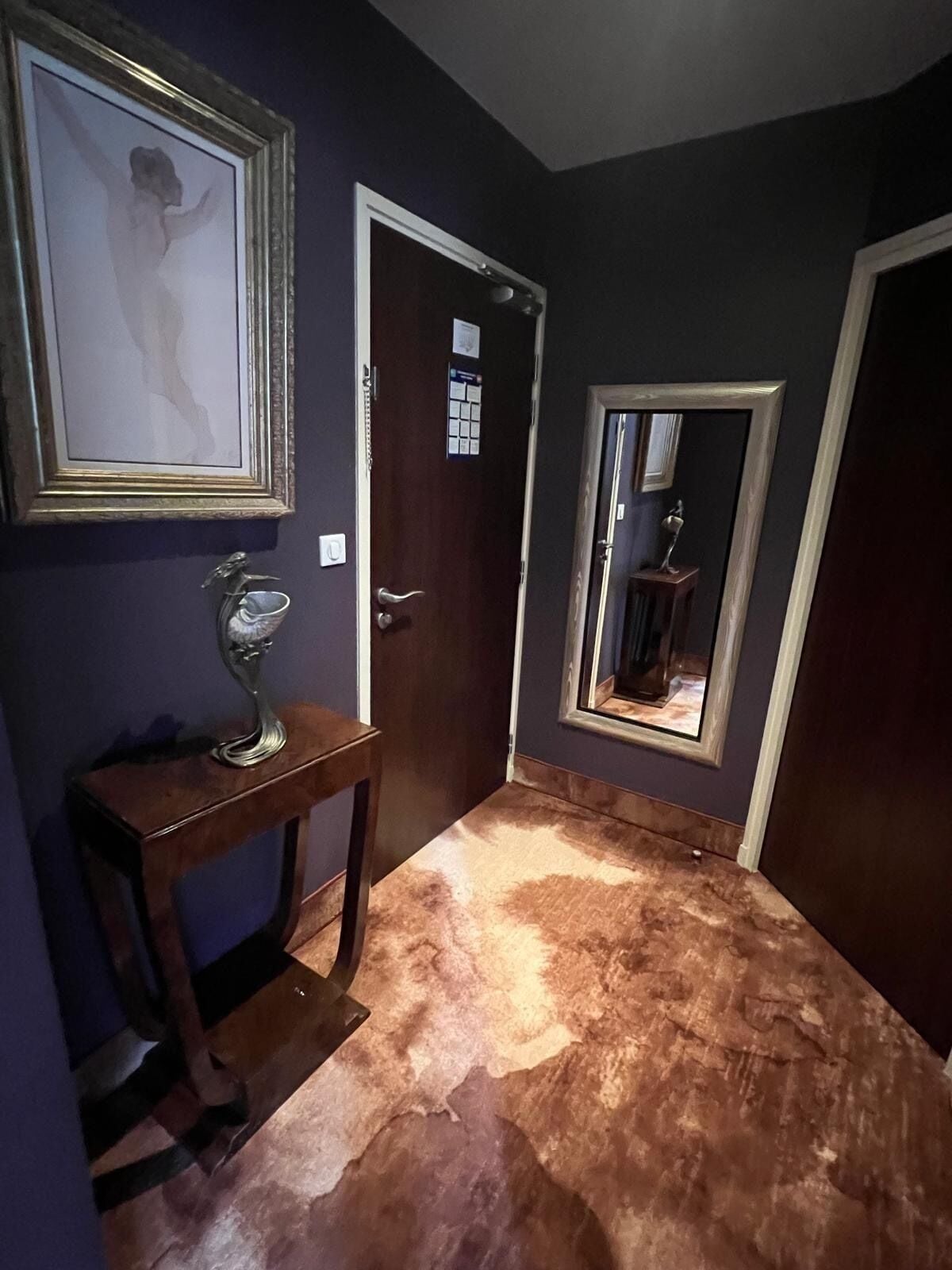 Um corredor com chão de mármore, uma porta com espelho e um quadro na parede.