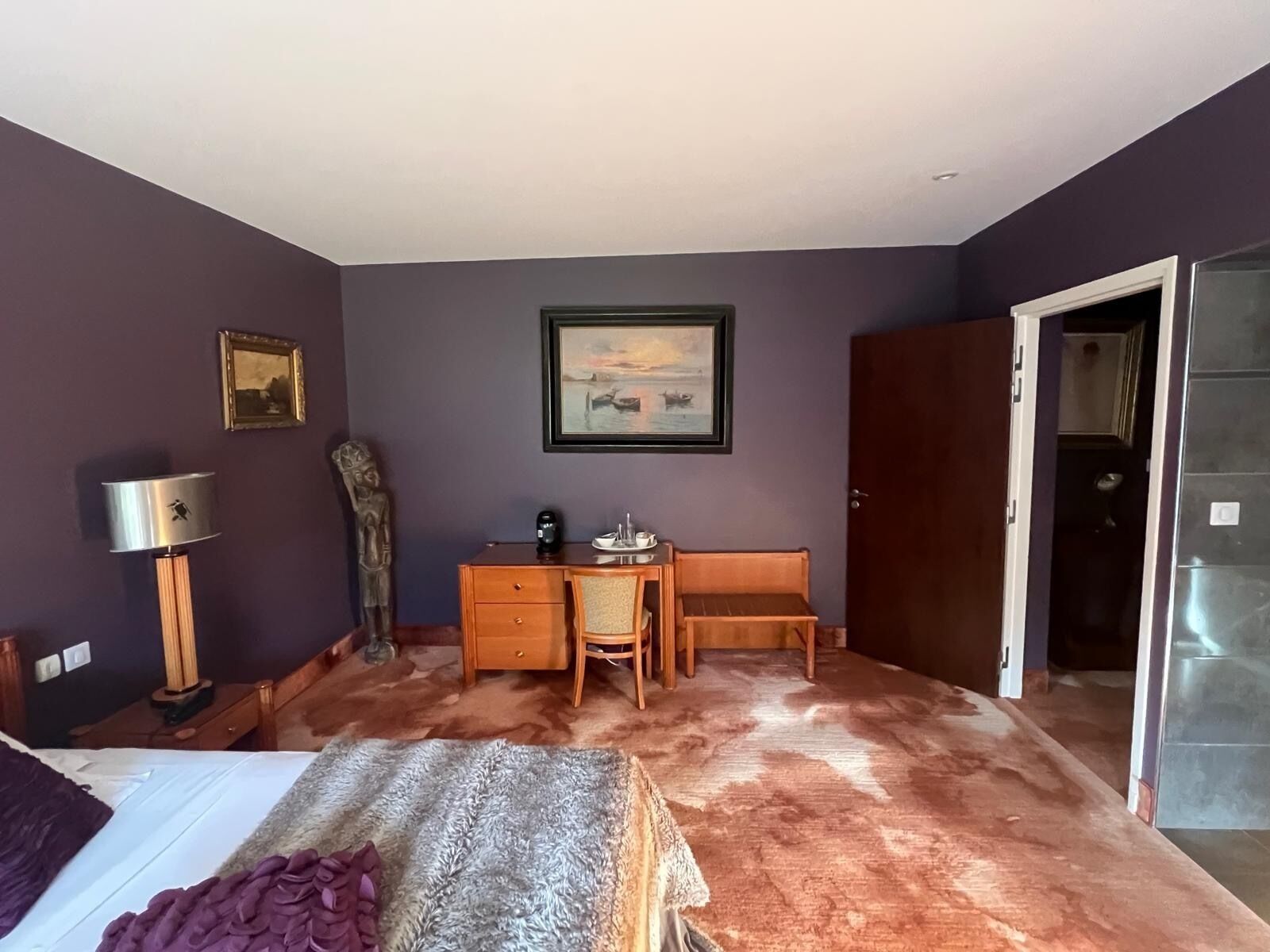Quarto com cama, escrivaninha, cadeira, abajur e porta.