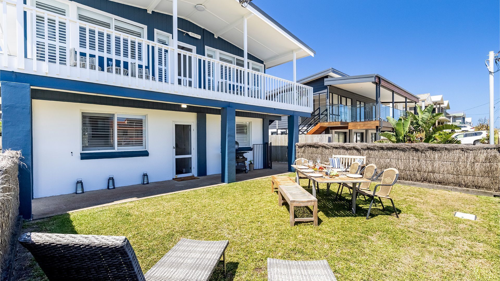 A two-story house with a covered patio, a dining area with outdoor furniture, and a view of neighboring buildings.