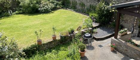 A well-maintained garden with a grassy lawn, potted plants, a barbecue area, and a stone wall.