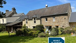 Un bâtiment en pierre doté d’un toit en pente, entouré d’un jardin bien entretenu. Une pancarte indique qu’il s’agit d’un lieu touristique.