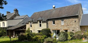 Un bâtiment en pierre doté d’un toit en pente, entouré d’un jardin bien entretenu. Une pancarte indique qu’il s’agit d’un lieu touristique.