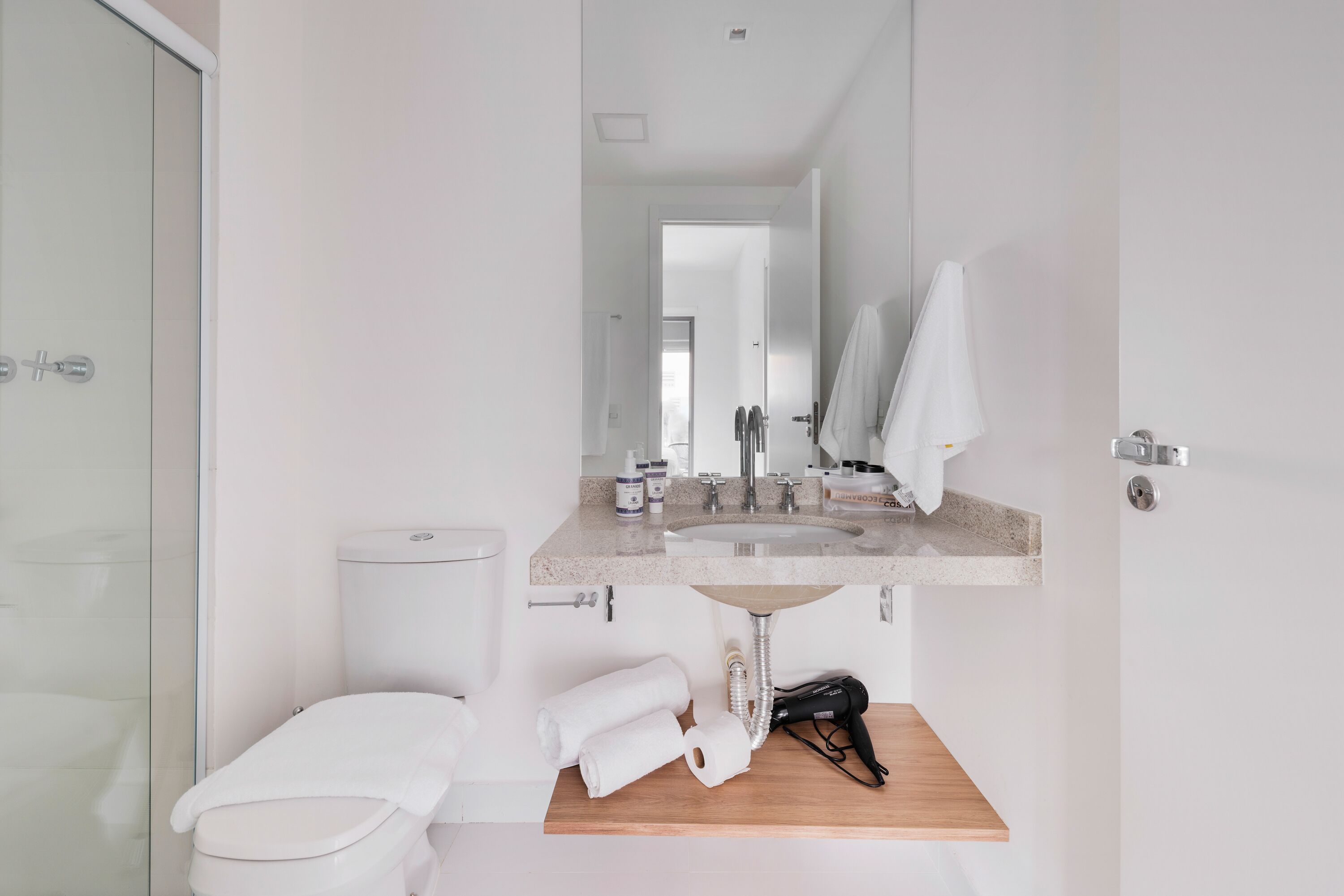 A modern bathroom with a toilet, sink, and mirror. There are towels and a hairdryer on the sink counter.