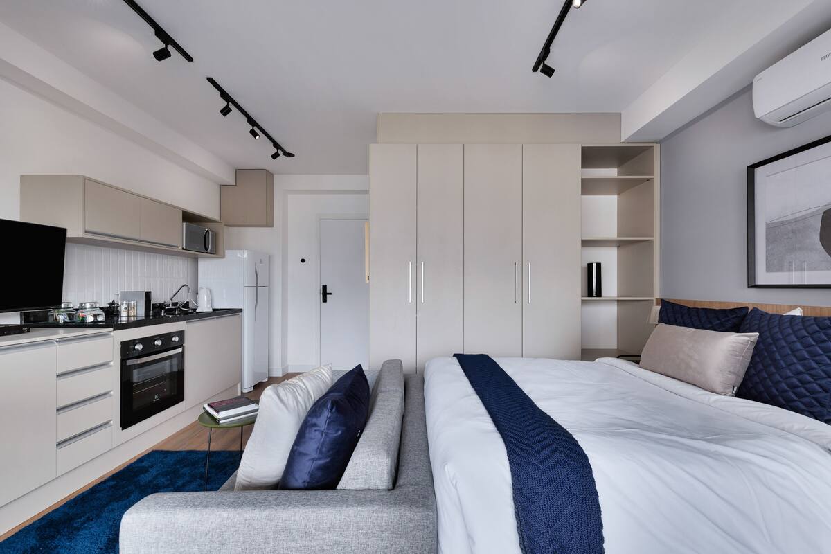 Un dormitorio moderno con una cama grande, armario empotrado, kitchenette y televisor de pantalla plana.