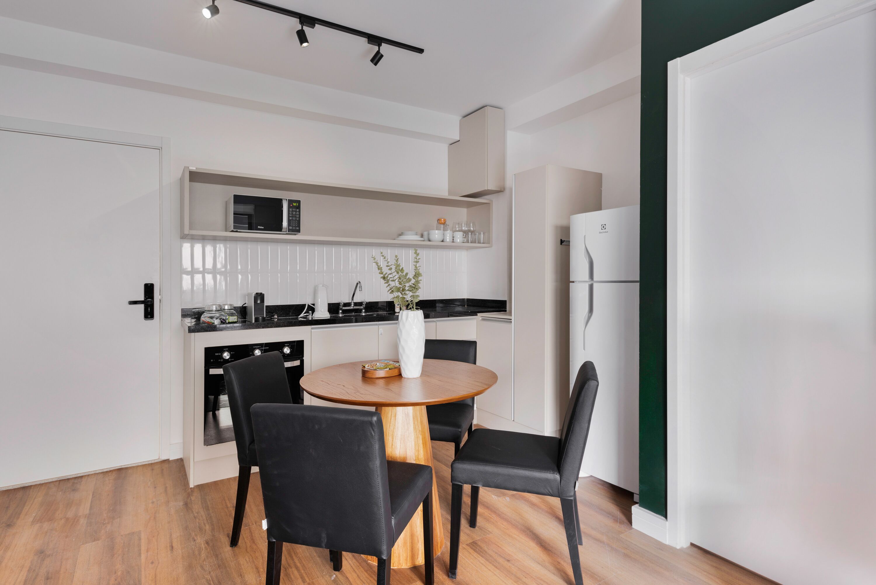A modern kitchen with white cabinets, a microwave, and a refrigerator. There is a dining table with four chairs and a vase with flowers.
